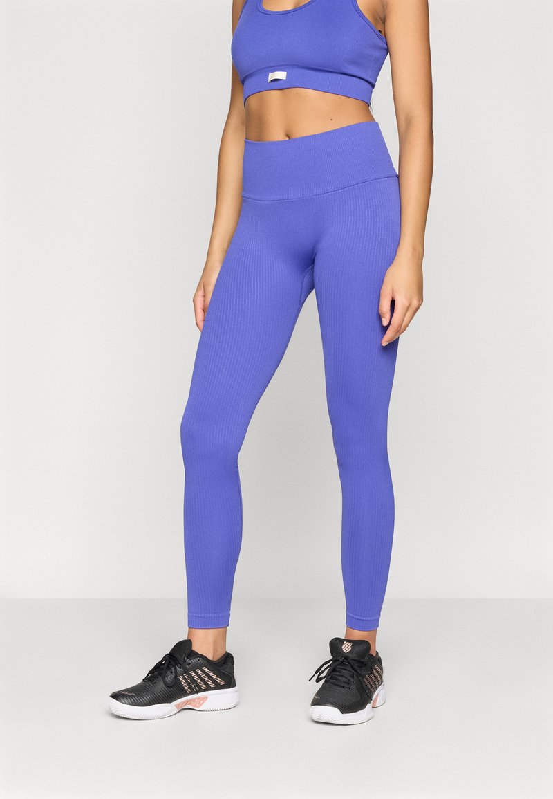 Ljubičasti rebrasti atletski crop top i helanke visokog struka u kombinaciji s crnim sportskim cipelama s ružičastim akcentima i mrežastim detaljima.