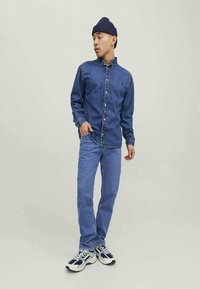 Denimskjorta, blå; knäppt fram, långärmad med kontrasterande tyg vid kragen. Blå jeans, ledig passform. Vita och marinblå sneakers, tjocka sulor.