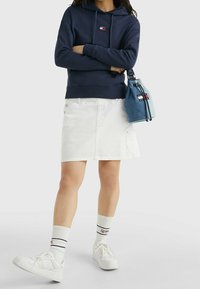 Felpa con cappuccio blu della marina, gonna di denim bianca, sneakers bianche e borsa a tracolla blu. Sono visibili calzini con dettagli neri e rossi.