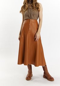 Brown leather midi skirt with a flared shape, featuring a button front and side pockets. Paired with brown knee-high boots.