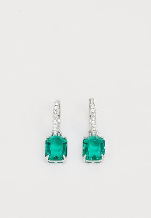 Boucles d'oreilles en argent avec des pierres précieuses rectangulaires vertes et de petites pierres claires le long des crochets sur un fond clair.