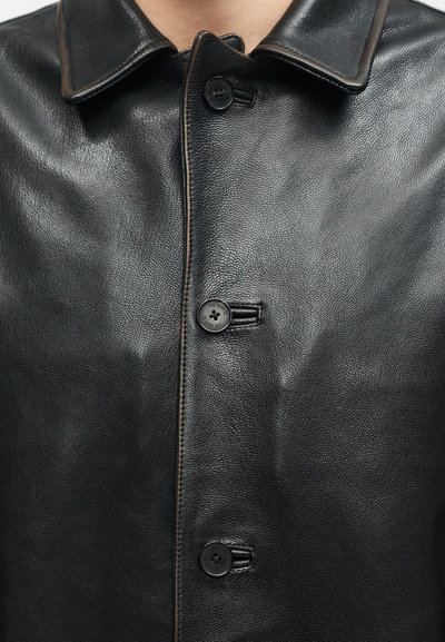 Μαύρο δερμάτινο μπουφάν με τρία μαύρα κουμπιά κουμπωμένα, διαθέτοντας διπλωμένο γιακά και λείο, απαλό φινίρισμα.