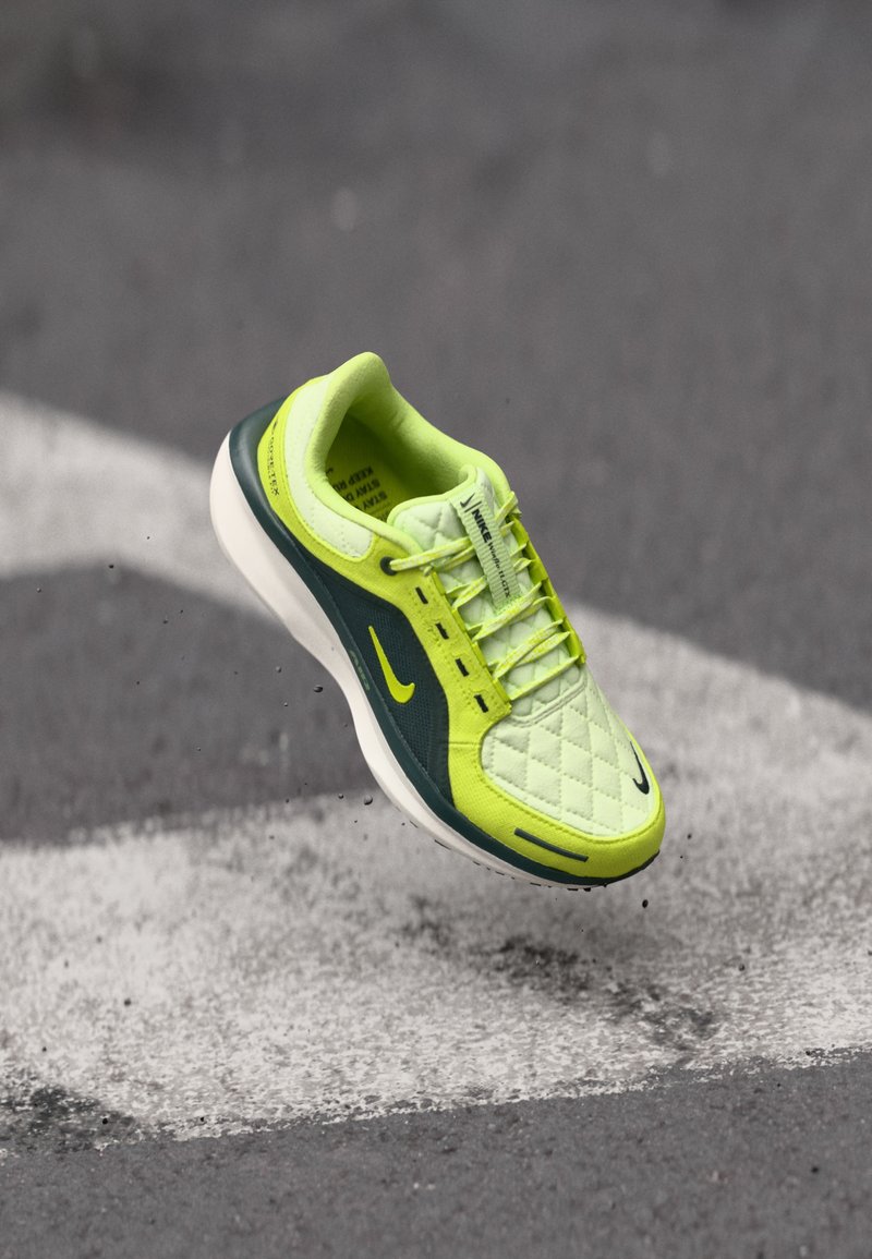 Limoengroene sneaker met een geborduurd bovenwerk, donkergroene accenten, witte zool en zichtbare zwarte Nike-swoosh; heeft een vetersluiting en een gestructureerd oppervlak.