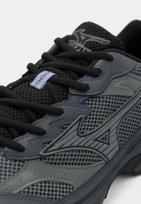 Gray athletic shoe featuring a mesh upper, black laces, and a textured design with a logo accent. Treaded sole for traction.