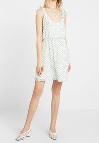 Světle zelené květinové šaty s kulatým výstřihem, zavázanými ramínky a elastickým pasem. Látka má měkkou texturu a volný střih.