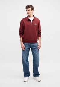 Μπέρμπερι μπλούζα quarter-zip με πλεκτές μανσέτες, που διαθέτει λογότυπο. Συνδυασμένη με ανοιχτό μπλε jeans σε χαλαρή γραμμή και λευκά αθλητικά παπούτσια.