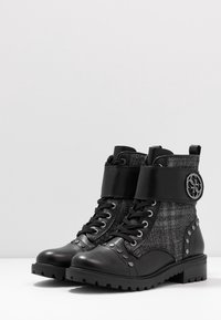 Zwarte enkellaarsjes met textiel en leren panelen, voorzien van metalen studs, vetersluiting aan de voorkant en een merkband rond de enkel.
