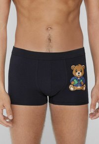 Černé bavlněné boxerky s potiskem medvěda v modré bundě, který drží peníze. Mají přiléhavý střih a elastický pas.