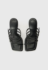 Des sandales en cuir noir présentent un design à bout carré avec plusieurs fines sangles. La texture est lisse, avec une semelle intérieure rembourrée pour le confort.