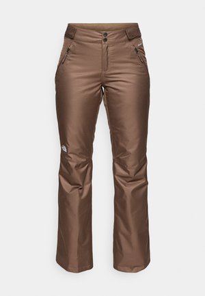 Pantaloni de schi impermeabili de culoare maro, cu o textură netedă, două buzunare laterale cu fermoar și un tiv în contrast. Prezintă un logo pe partea inferioară a piciorului.