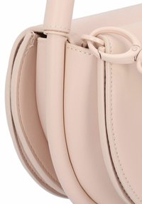 Bolso de cuero rosa claro con forma redondeada, costuras visibles y un detalle de metal en el asa lateral. Textura suave.