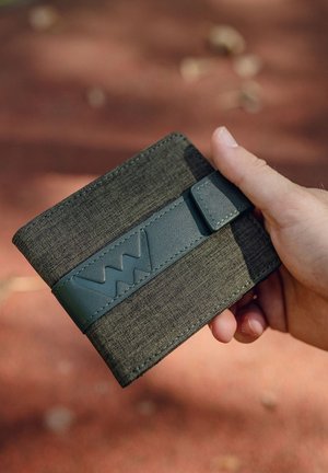 Green fabric wallet with a textured surface and a matching strap featuring an embossed logo. Slim rectangular shape with rounded edges.