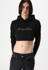 Black cropped hoodie featuring a drawstring and "Boiler Room" in silver embroidery. Paired with fitted black jeans, showcasing a sleek silhouette.