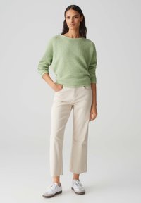 Hellgrüner, strukturiert geschnittener Pullover, locker sitzend, runder Halsausschnitt. Off-White, gekürzte Hosen mit fransigem Saum. Weiße Sneakers mit braunen Sohlen.