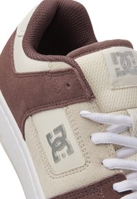 Sneaker marron et crème avec une tige en nubuck et mesh, lacets blancs et un accent logo argenté. Bout arrondi et col rembourré pour le confort.
