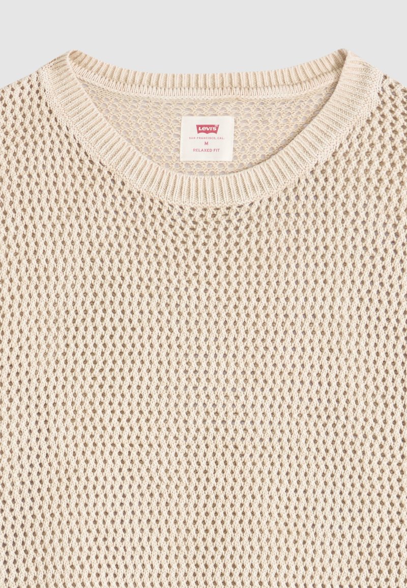 Pull beige tricoté col rond avec un motif en maille ouverte et une étiquette Levi's indiquant une taille moyenne et une coupe décontractée.