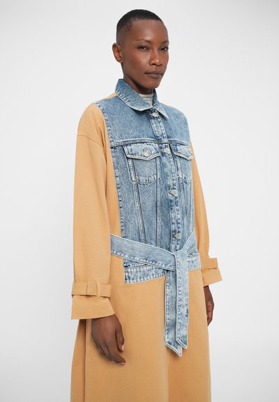Robe en denim et beige avec un buste en denim bleu clair, un col de chemise et une ceinture à nouer. Les manches longues disposent de poignets réglables.