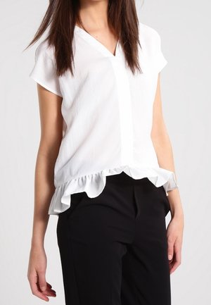 Blusa blanca de manga corta, con escote en V y un dobladillo con volantes. Tela ligera con una textura suave, combinada con pantalones negros.