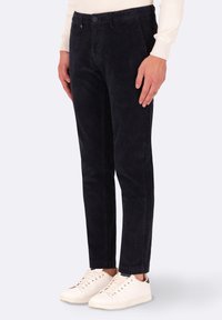 Pantaloni di velluto a coste blu navy con vestibilità slim, caratterizzati da una trama a coste verticali, tasche frontali e chiusura con un singolo bottone, abbinati a sneakers bianche.