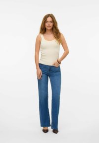 Beige, åtsittande linne kombinerat med blå, raka jeans. Outfiten fulländas med bruna skor med spetsig tå och ett träarmband.