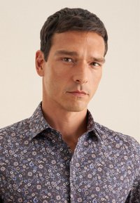 Bloemmotief shirt in donker marineblauw met kleine paarse en blauwe bloemen. Heeft een klassieke kraag en knoopsluiting. Van katoen.