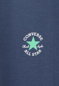 Jūras spēku īsām piedurknēm T-krekls ar apaļu balti-mint zaļu grafiku, kurā ir teksts "CONVERSE Chuck Taylor ALL STAR" un zvaigžņu simbols.