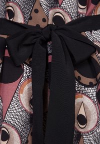 Tessuto a fantasia con disegni circolari e triangolari nelle tonalità di rosa, marrone e nero; presenta una cintura di stoffa nera annodata a fiocco.