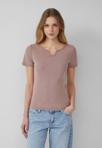 Geribbelde roze T-shirt met korte mouwen en een V-hals, voorzien van subtiele stikdetails. Gecombineerd met lichtblauwe relaxed-fit jeans.