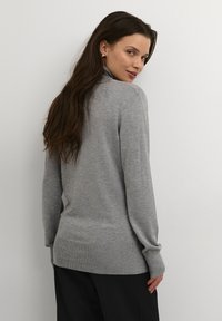 Grå turtleneck sweater lavet af blødt, let stof, med lange ærmer og en tætsiddende kant, vist fra bagsiden mod en ensfarvet baggrund.