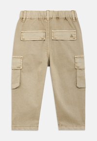 Bež hlače s pritiskači z elastiko na pasu, štiri žepi in podvitimi zaključki na nogah. Iz mehke, trpežne tkanine s gladko teksturo.