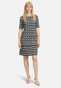 Sukienka z krótkim rękawem w granatowym kolorze z kremowym falistym wzorem. Gładki materiał, długość poniżej kolan, warstwowy krój. Połączona z białymi sandałami na ramiączkach.