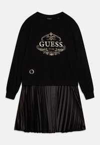 Schwarzes Sweatshirtkleid mit einem goldenen, gestickten "GUESS"-Logo, ergänzt durch einen gefütterten, satinähnlichen schwarzen Rock und einem silbernen, runden Akzentdetail.