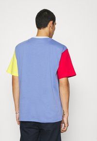 Krátký rukáv tričko s modrým tělem, žlutým levým rukávem, červeným pravým rukávem a kulatým výstřihem; vyrobeno z měkké bavlněné látky.