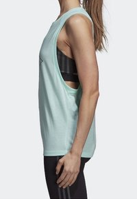 Top de tirantes sin mangas de color verde menta con un ajuste relajado, textura suave, sisas amplias y escote redondeado, usado sobre un sujetador deportivo negro.