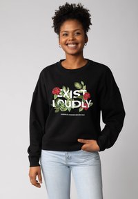 Zwarte sweater met bloemmotief met rode rozen en groene bladeren, tekst "EXIST LOUDLY" in wit, geribde halslijn en manchetten.