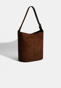Braune Wildleder-Bucket-Bag mit einer geschwungenen Silhouette und einem schwarzen Ledergriff. Verfügt über eine dezente Nahtdetail entlang der Vorderseite.