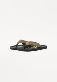Tongs en caoutchouc avec une sangle tissée olive verte texturée et un accent rose, équipées d'une semelle noire avec un logo imprimé. Design plat, style décontracté.