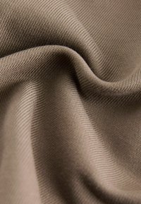 Brauner Stoff mit einer weichen Textur und geripptem Muster, der sanfte Falten und Kurven aufweist. Glattes Aussehen mit einem dezenten Glanz.