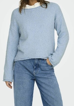 Light blue textured sweater with a wide neckline, long sleeves, and raw edges, paired with high-waisted blue jeans.