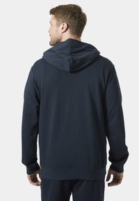 Marineblauwe pullover hoodie met een zachte textuur, beschikt over een ruime capuchon, geribbelde manchetten en een rechte zoom, ontworpen voor comfort.