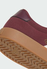 Burgundské semišové tenisky s hladkým burgundským koženým patním dílem, bílými akcenty a texturovanou gumovou podšívkou s vlnitým vzorem.