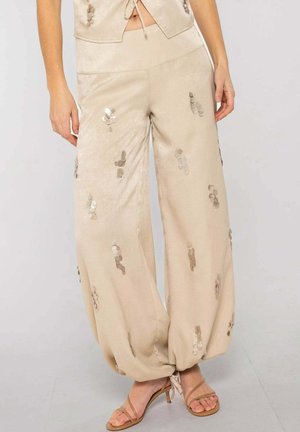Pantalones beige de pierna ancha con grupos de lentejuelas, recogidos en los tobillos, usados con sandalias beige de tacón alto y tiras.