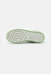 Nike sneaker sole featuring a smooth white base, textured light green accents, and distinct circular tread pattern for traction.