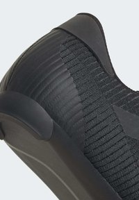 Gros plan sur une basket noire à enfiler présentant un tissu en maille texturée et une semelle en caoutchouc lisse avec une languette au talon.
