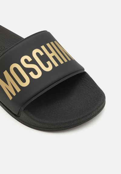 Schwarze Slipper-Sandalen mit einem breiten Riemen, auf dem der Text "MOSCHINO" in goldener Schrift gedruckt ist. Strukturierte Fußbett und glatte Laufsohle.