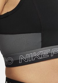 Sort og grå sports-bh med et struktureret mønster på den grå del, udstyret med et bredt sort linning med "NIKE PRO" trykt i hvidt.