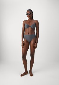 Grå bikinitopp med formarade kupor, tunna axelremmar och högmidjade bottnar. Slät textur, minimalistisk design och inga mönster.
