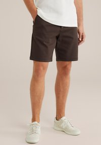 Bruine katoenen shorts met een klassieke pasvorm, zijzakken en een gladde textuur, gecombineerd met witte sportschoenen.