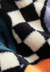 Mehrfarbige, flauschige Decke mit einem schwarz-creamfarbenen karierten Muster und Akzenten in Türkis und Orange. Weiche Textur mit tiefem Flor.
