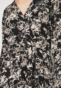 Black wrap dress with a textured fabric, featuring a light beige abstract pattern. The design includes long sleeves and a fitted waistline.